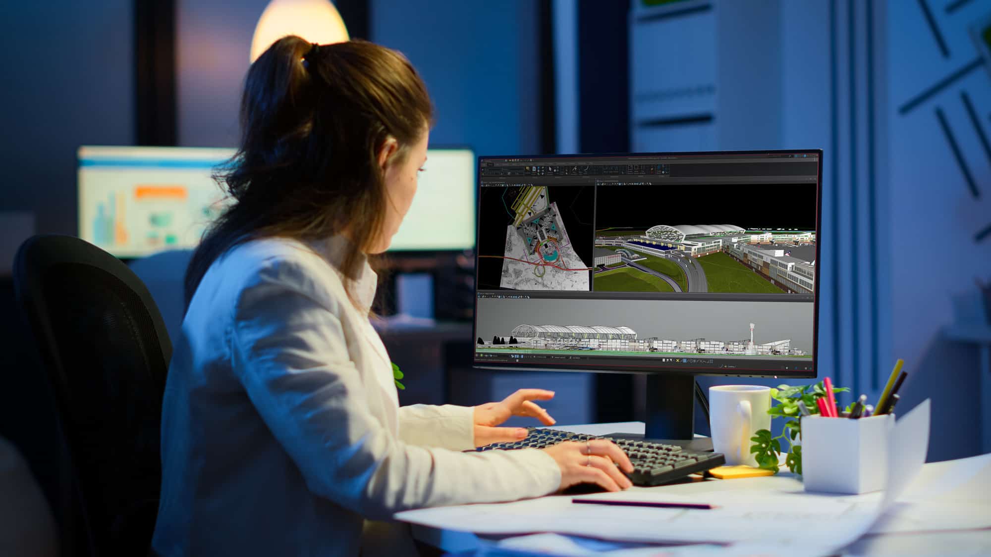 A woman working on a cad project on her computer in an office at night.