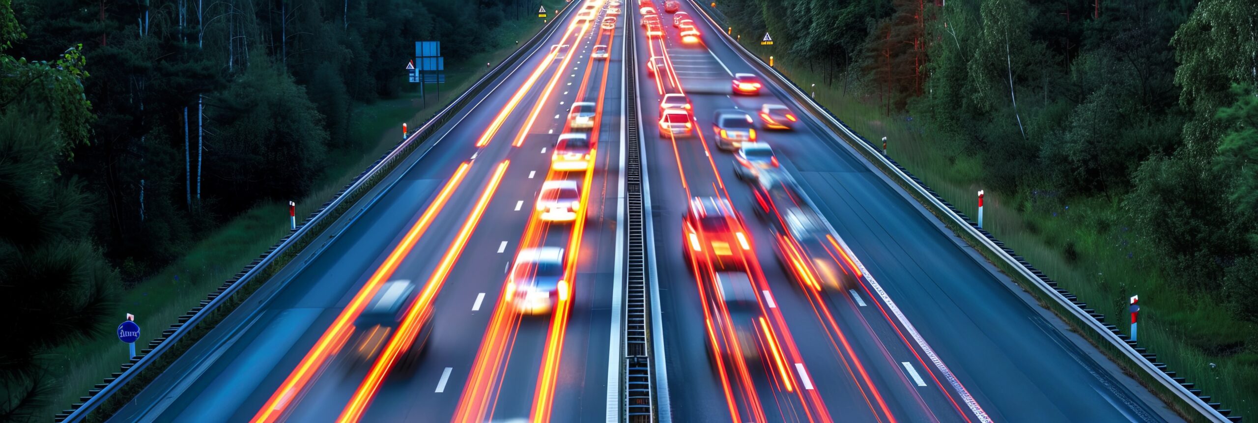 A long-exposure photo of a busy highway at dusk, showing the blurred motion of car lights in both directions, with surrounding trees and a clear sky—a perfect example of efficient roadway design managed by state and local authorities.